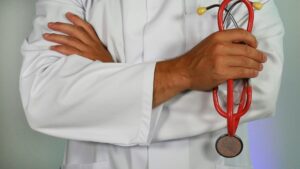 person standing with arms folded wearing a medical coat, holding a stethoscope