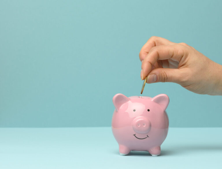 ceramic pink piggy bank and hand throwing a coin inside, finance savings concept, copy space