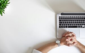 computer on white desk with hands foleded on top