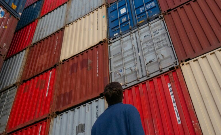 Man in Black Jacket looking at shipping containers at port