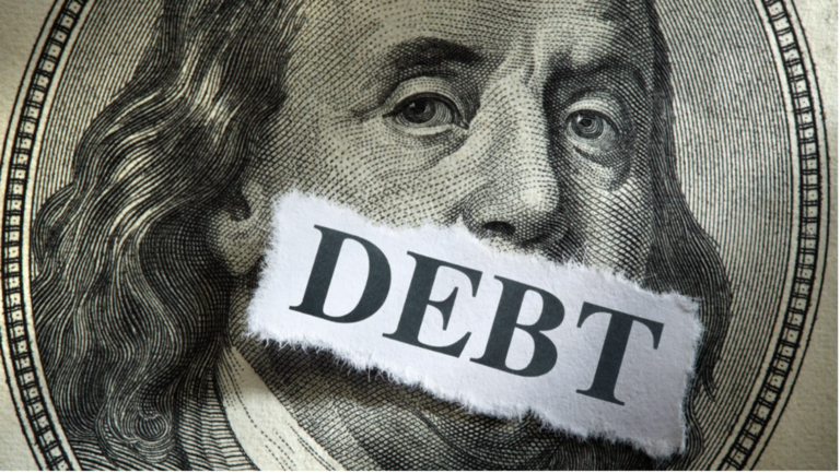 Close-up of Benjamin Franklin’s face on a U.S. hundred-dollar bill with a torn piece of paper labeled “DEBT” covering his mouth, symbolizing the silencing or suppression caused by national debt.