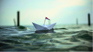 a paper boat floating in the open sea during rough waters trying to stay afloat
